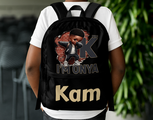Black backpack with a melanin boy cartoon character in front of a brick wall, wearing sneakers and jacket, with text “PRE K I’M ONYA” and a personalized name at the bottom. Worn by a young boy.
