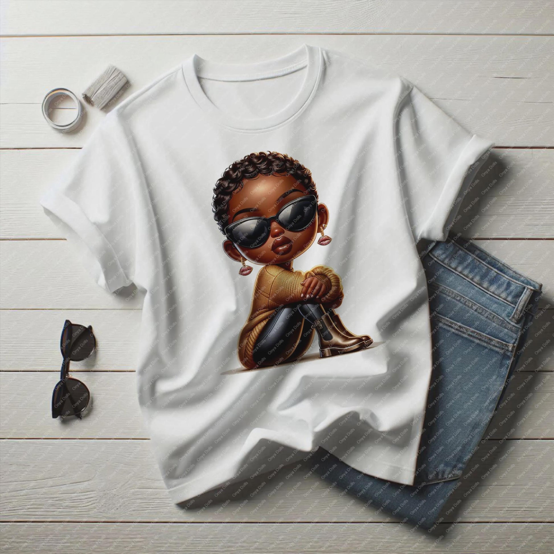 White t-shirt with a graphic of a child wearing sunglasses, accompanied by sunglasses and jeans on a wooden surface.